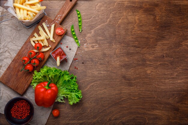 Patate fritte in una griglia con ketchup, insalata e pomodorini sul tavolo marrone in legno