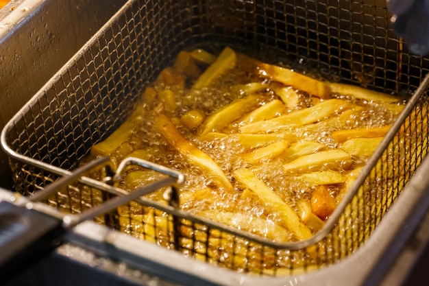 フライパンのバスケットに熱い油で揚げたフライドポテト料理