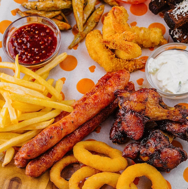 Photo french fries potatoes with onion rings sausages croutons and spicy chicken legs