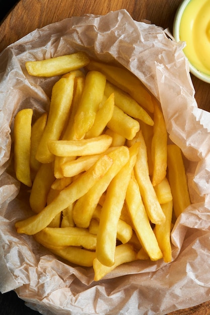 French fries Tasty French fries server on parchment paper on wooden cutting board with tomato and cheese sauce on wooden table background Diverse Keto Dishes Fast food and unhealthy food concept