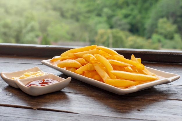 Patatine fritte su un piatto bianco servite con ketchup di peperoncino e maionese sfocatura dello sfondo naturale