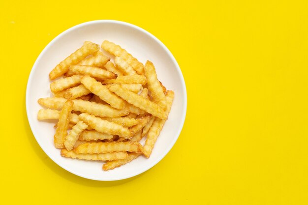 French fries in white plate on yellow background.