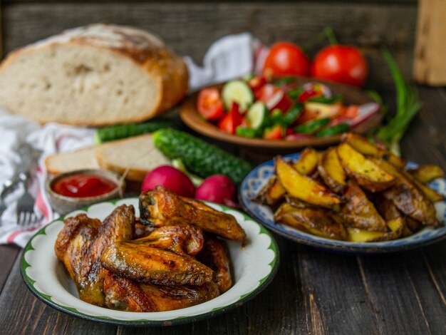 French fries, wings, salad, vegetables, bread on an old wooden background. Rural dinner, summer picnic. Top view. Flat lay.