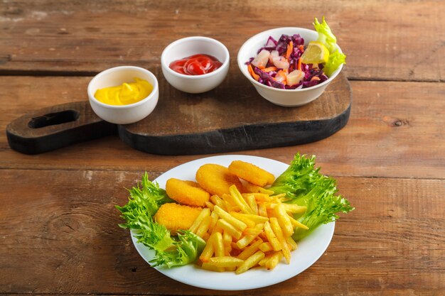 Картофель фри с куриными наггетсами рядом с сырным соусом и кетчупом в соуснике и салат на деревянных досках. горизонтальное фото