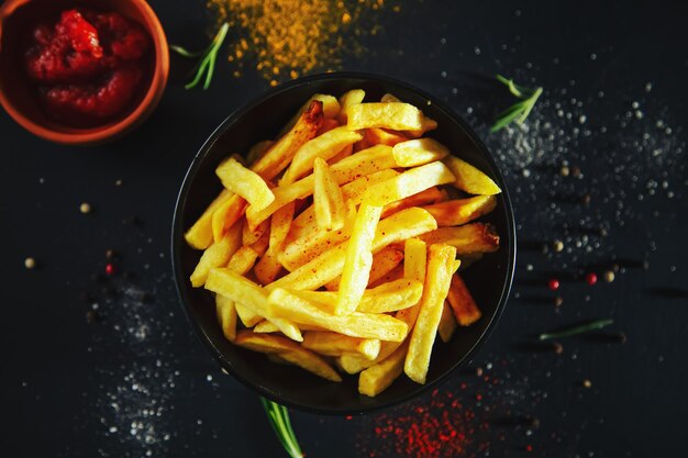 French fries with ketchup and spices on a black background