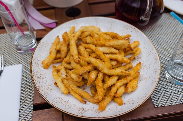 パウダーチーズとマヨネーズソースを添えたフライドポテトは、食べ物の背景や食感のために黒いプレートで提供されます。