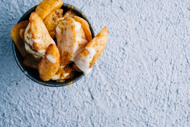 French fries with spices and sauce in a metal bowl on blue table background