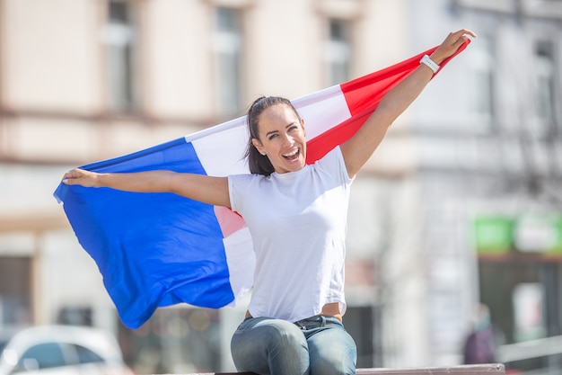 Photo french girl holds a flag behind her, celebrating outdoors.