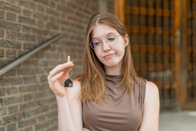 french girl with glasses holding home keys at outdoors with sad expression