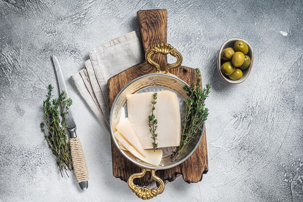 French hard goat cheese in a skillet with herbs White background Top view