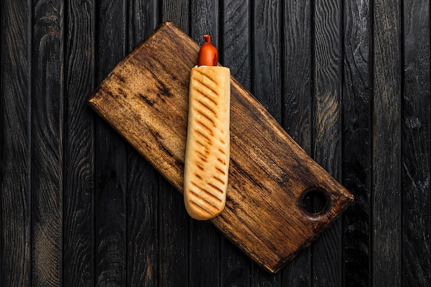 French hot dog in a crispy bun served on wooden board on dark wooden backdrop