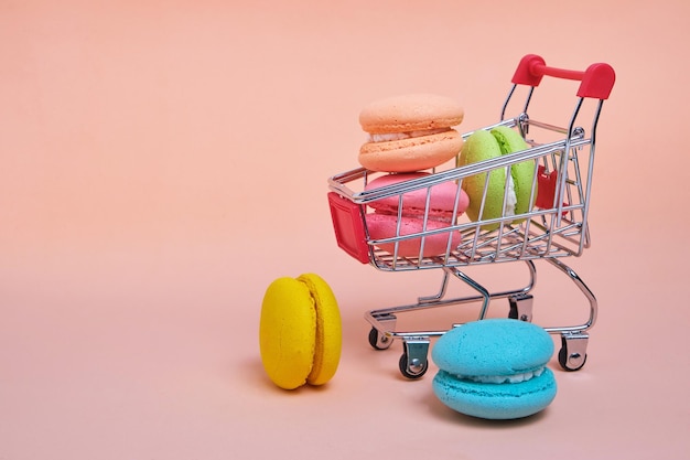 French macarons cookies in a shopping cart on a pink background