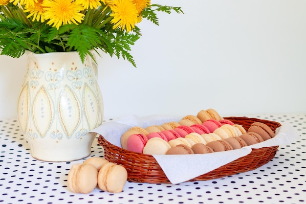 French macaroons in a basket on the table and a bouquet of yellow dandelions in a jug