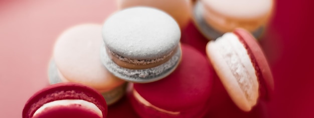 ワインレッドの背景にフランスのマカロンパリのシックなカフェデザート甘い食べ物と高級菓子ブランドの休日の背景デザインのためのケーキマカロン