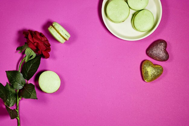 French pistachio macarons with red rose flower and heart glitters on purple background