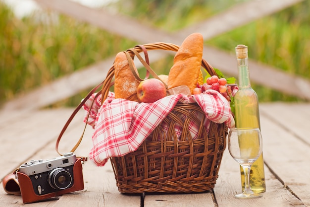フランスの地方ピクニック。食品、レトロなカメラ、湖で木製の桟橋にワインのボトルとレトロなスタイルのピクニックバスケット