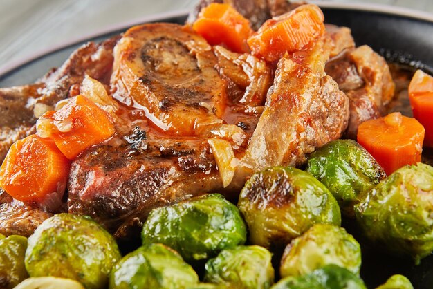 French recipe Brussels sprouts with esobuco meat on black plate on wooden background