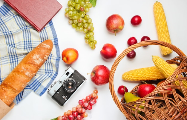 French retro style picnic. Basket with fruits and vegetables, retro camera, book, baguette and other picnic food white background.