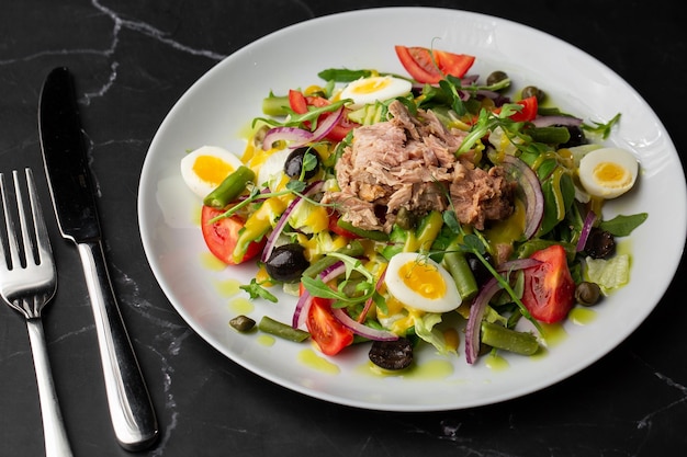 French salad Nicoise with tuna egg green beans tomatoes olives lettuce onions and anchovies on a gray background Healthy food