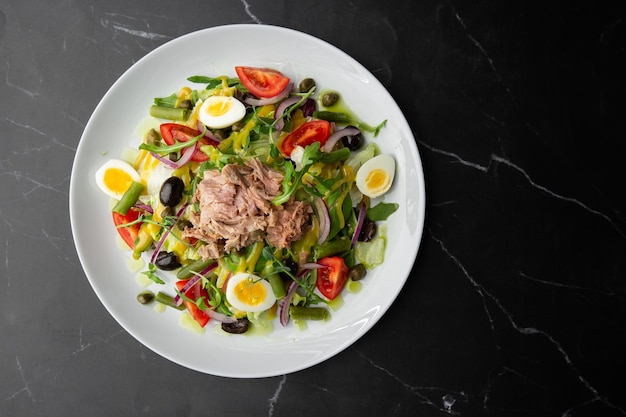 French salad Nicoise with tuna egg green beans tomatoes olives lettuce onions and anchovies on a gray background Healthy food