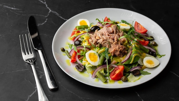 French salad Nicoise with tuna egg green beans tomatoes olives lettuce onions and anchovies on a gray background Healthy food