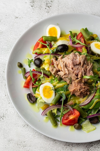 French salad Nicoise with tuna egg green beans tomatoes olives lettuce onions and anchovies on a white background Healthy food