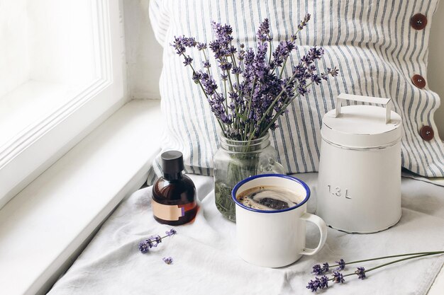 French summer still life Cup of coffee lavender flowers bouquet essence oil bottle on windowsill Feminine styled stock photo floral composition with Lavandula officinalis herbs Rustic scene