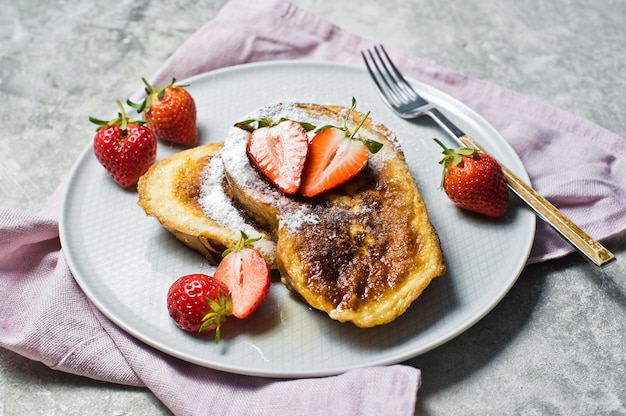 French toast with strawberries and maple syrup on a gray plate. 