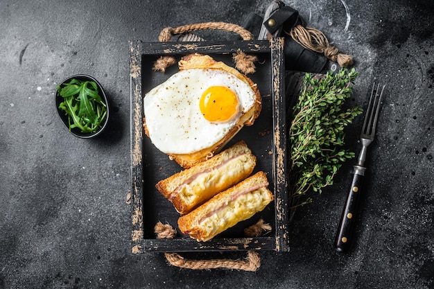 French toasts croque monsieur and croque madame with sliced ham, melted emmental cheese and egg. Black background. Top view.