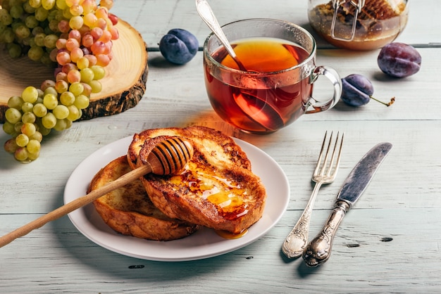 French toasts with honey fruits and tea over white wooden