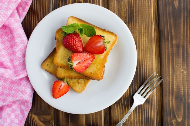 French toasts with strawberries in the white plate on the brown wooden table.Top view.Copy space.Closeup.