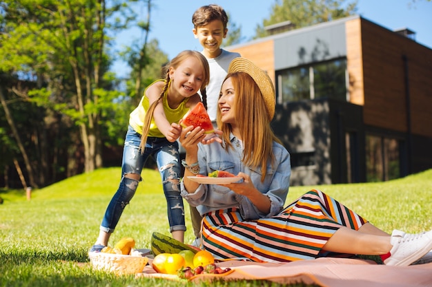 Fresh air. Cheerful pretty mother smiling and giving watermelon to her kids