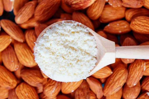 Fresh almond flour in a wooden spoon on an almond background closeup