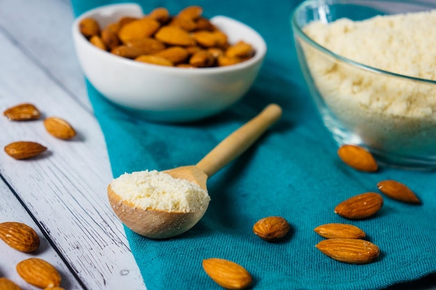 Fresh almond flour in a wooden spoon with almonds on a white wooden table copy space