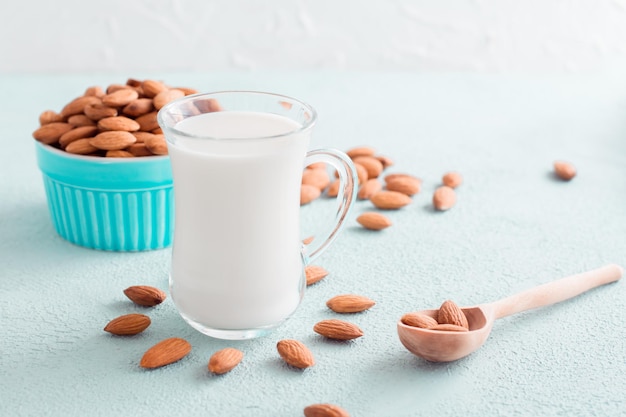 Latte di mandorla fresco in un bicchiere e mandorle in un cucchiaio di legno su sfondo chiaro. alimentazione alternativa, fonte di vitamine