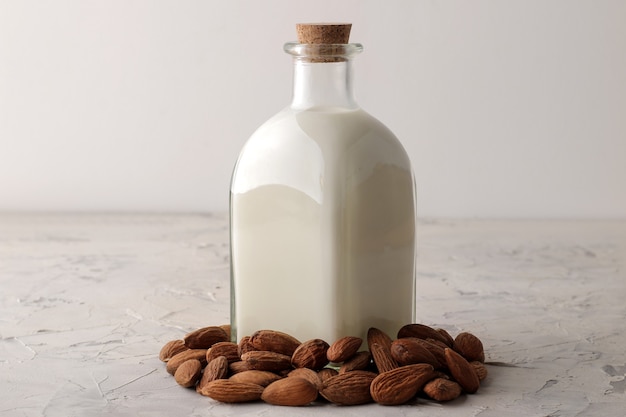 Fresh almond milk in a glass bottle and almond nuts on a light background