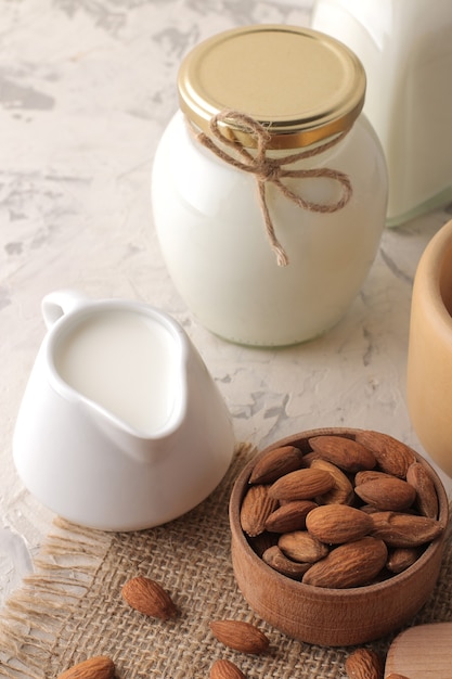 Fresh almond milk in a milk jug and almond nuts on a light background