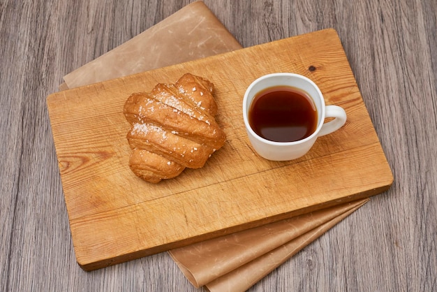 Fresh and appetizing croissant with a cup of coffee on a wooden\
surface