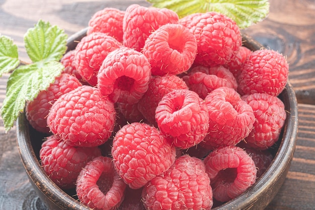 Fresh appetizing raspberries in bowl on a wooden table close up