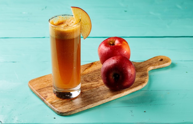 Свежий яблочный сок с сырыми яблоками подается в стакане, изолированном на разделочной доске, вид сбоку здоровый фруктовый сок