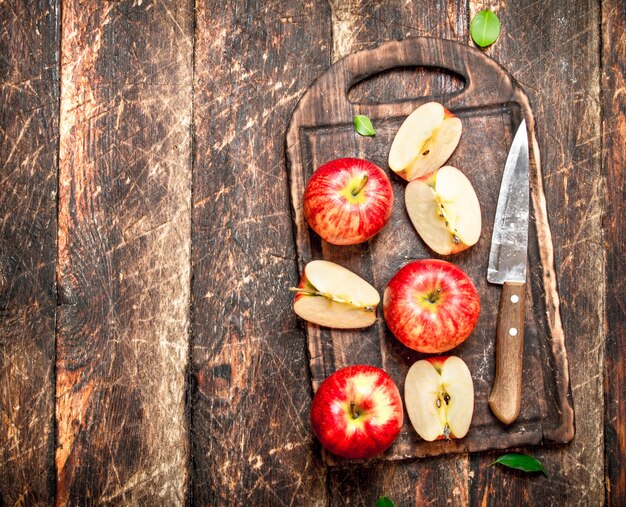 Свежие яблоки на разделочной доске с ножом. На деревянном столе.