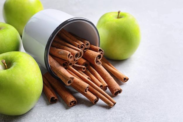 Fresh apples and mug with cinnamon sticks on table