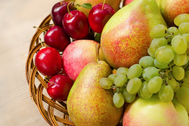 Fresh apples, pears, grapes and plums in a woven wooden plate