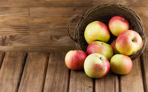 Fresh apples spill out of a basket on a wooden floor