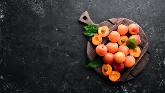 Fresh apricots with green leaves on a black background Rustic style Top view Free space for your text