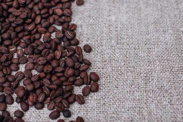 Fresh aromatic roasted coffee beans scattered on a beige burlap background Top view