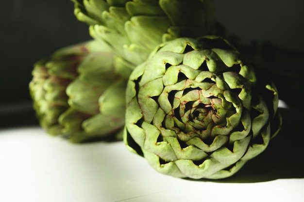 Photo fresh artichoke on a white wooden background with beautiful daylight shadow, close up. two raw organic artichoke flowers