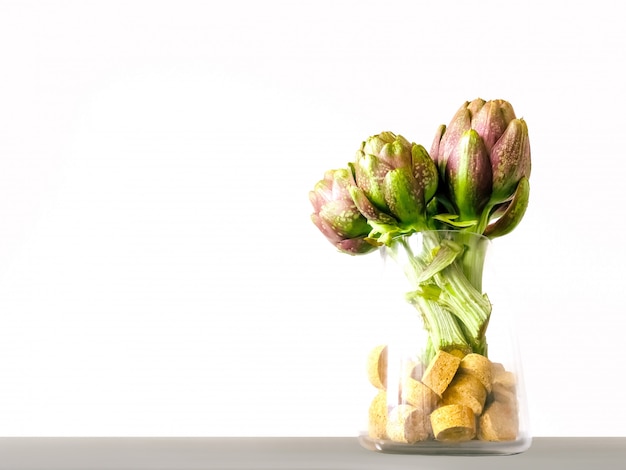 Fresh artichokes in glass vase on grey and white background. Organic artichoke flowers in vase with front view 