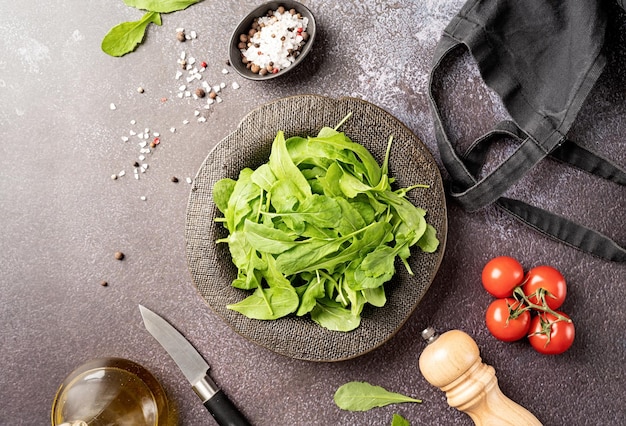 Fresh arugula leaves in black bowl with fresh vegetables copy space