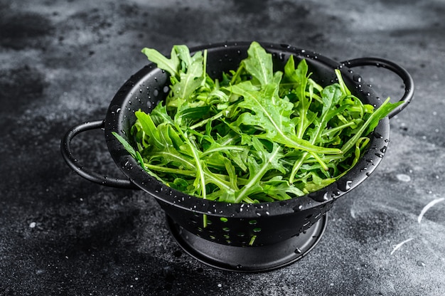 Fresh arugula leaves in a colander. Black surface. Top view